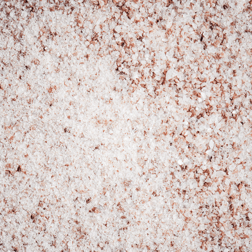 A close-up view of Himalayan salt, showcasing its coarse texture with shades of white and pink crystals spread over a flat surface.